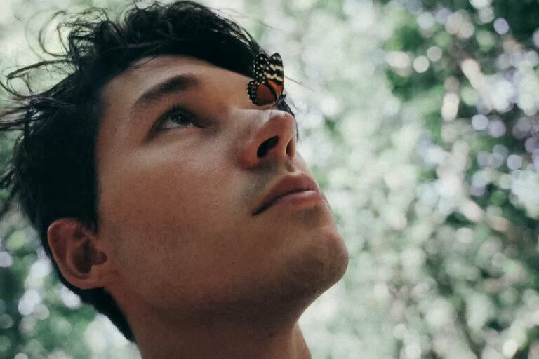 A man looks up in the sky, while a butterfly sits on his nose
